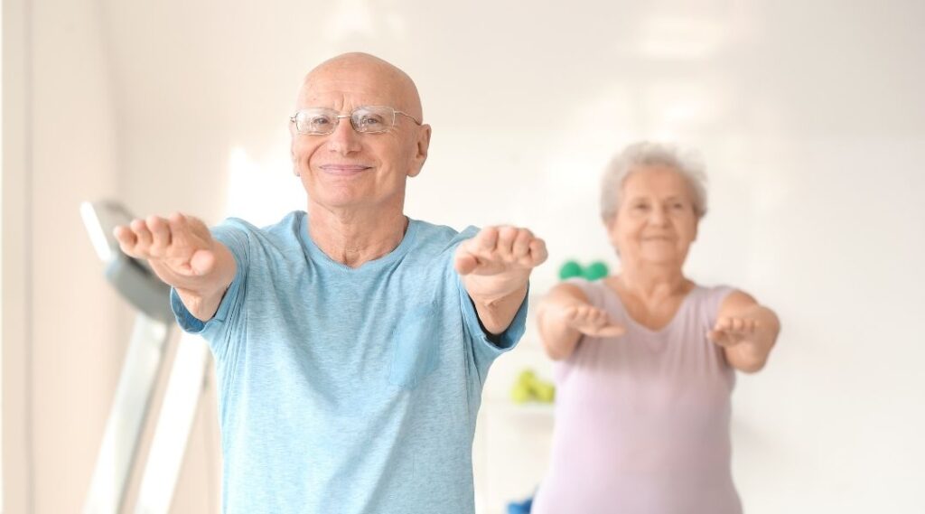 Deux-seniors-pratiquant-un-exercice-d'ouverture-des-bras-en-groupe-lors-d'une-séance-de-gym-douce