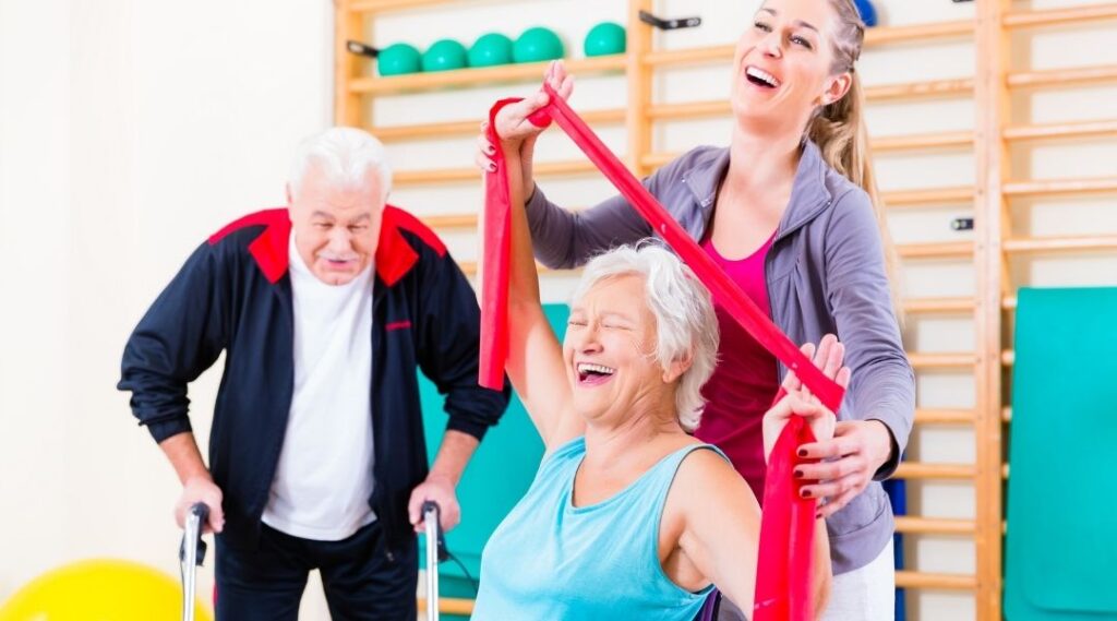 Intervenante-accompagnant-une-résidente-senior-dans-un-exercice-de-gym-douce-avec-elastique-en-établissement