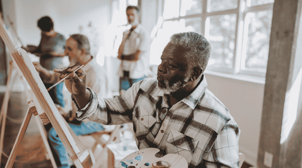 Homme-senior-peignant-sur-un-chevalet-avec-une-palette-lors-d-un-cours-d-art-en-atelier
